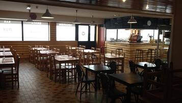 A restaurant with wooden tables and chairs, a bar area, and a visible kitchen counter.