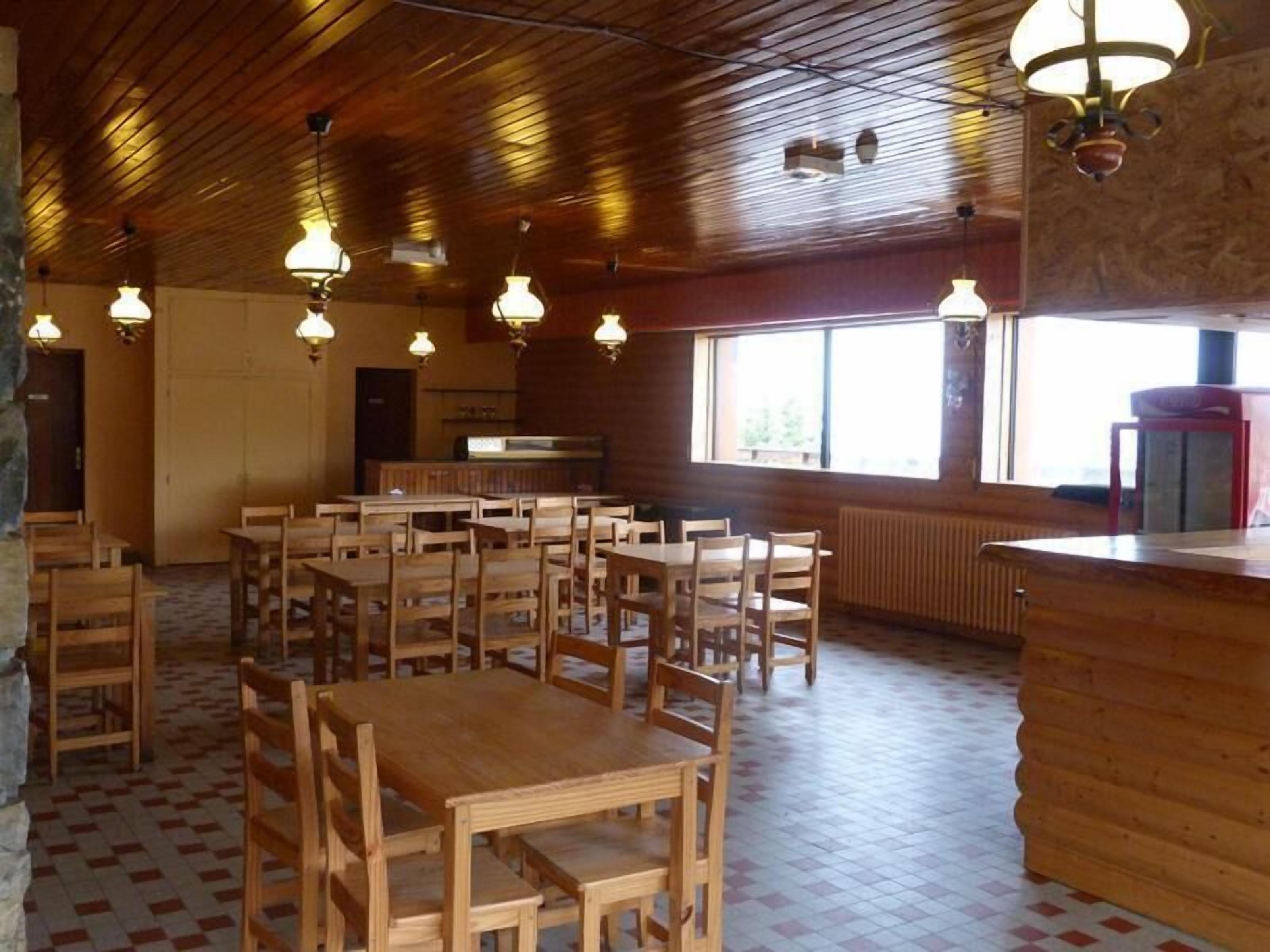 A spacious dining area with wooden tables and chairs, a counter with a cash register, and large windows allowing natural light.