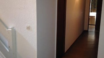 Un couloir étroit avec une porte en bois et un luminaire fixé au mur.