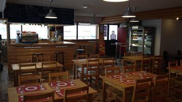 Un interior de restaurante con mesas y sillas de madera, una zona de bar y un refrigerador de Coca-Cola.
