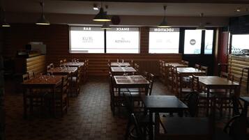 Un restaurant avec des tables et des chaises en bois, un sol carrelé et de grandes fenêtres sur lesquelles sont affichés les menus.