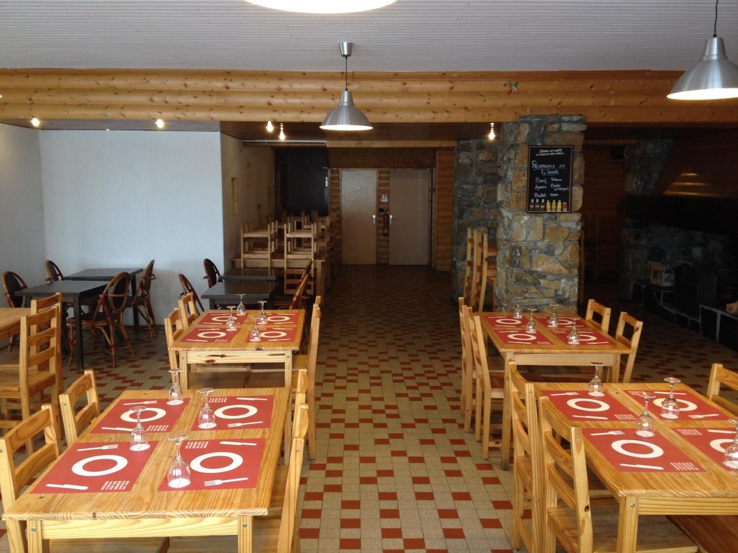 Ein Restaurant mit Holztischen und -stühlen, einer Steinsäule und einem Schachbrettboden.