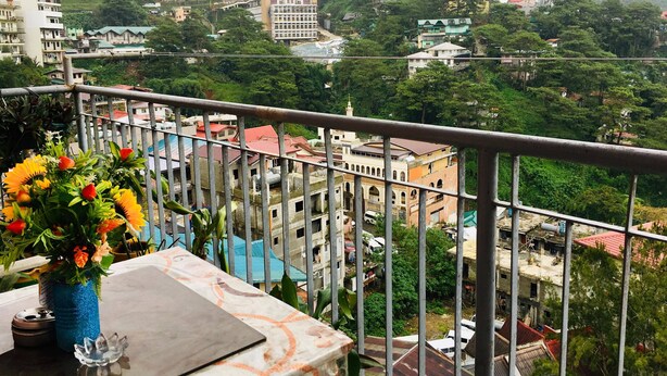 Un balcon offrant une vue sur un quartier résidentiel situé sur une colline, avec divers bâtiments et de la verdure.