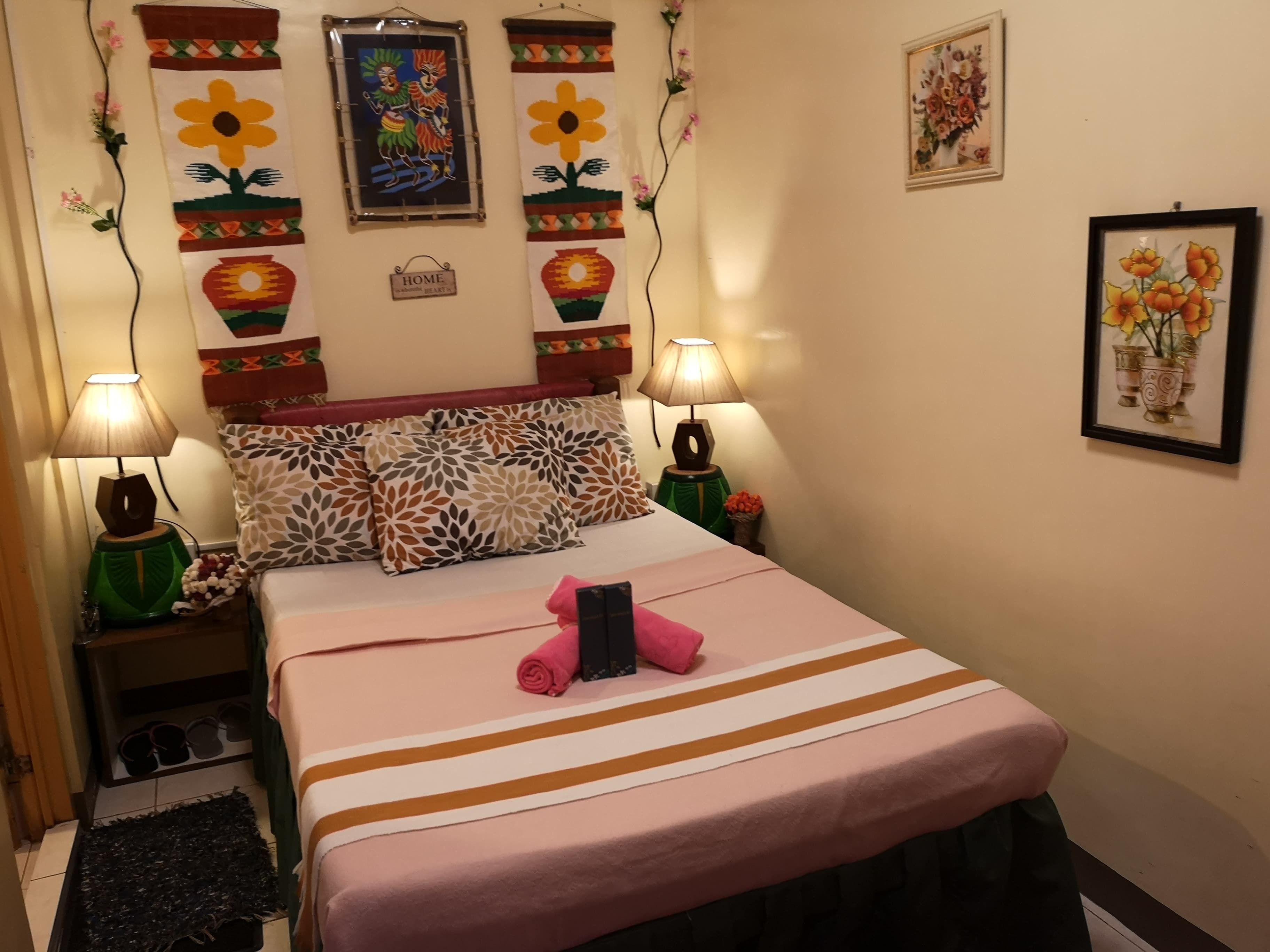 Un dormitorio ordenado con cama, almohadas y dos lámparas fijadas a la pared.