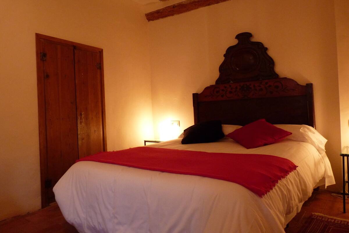 A bedroom with a wooden headboard, a bed with white and red bedding, a wooden door, and a nightstand with a lamp.