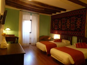 Une chambre avec deux lits, un bureau, une lampe et une tapisserie au mur.