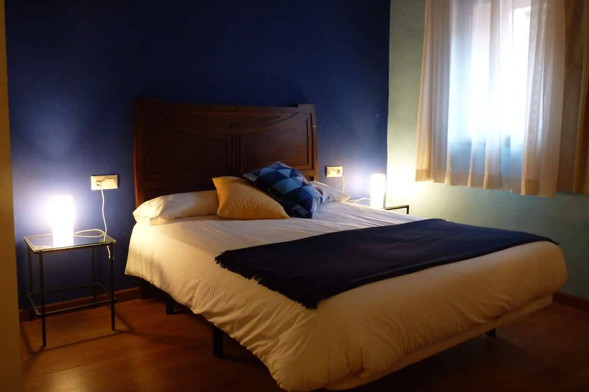 A bedroom with a large bed, two bedside tables, and a window with curtains.