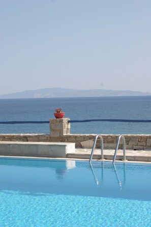 A swimming pool with a stone wall and metal railings, overlooking a body of water and distant mountains.