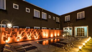 A pool area with lounge chairs, a wall with geometric patterns, and a building with windows and a door. - Pousada Armazem 26 (Tiradentes)