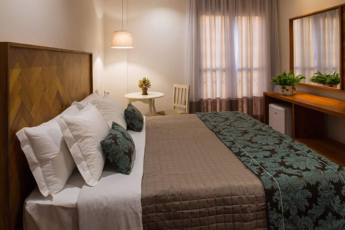 A neatly arranged hotel room with a bed, bedside table, chair, and a desk with a mirror.