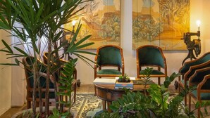 A cozy living room with a large plant, two green armchairs, a coffee table, and traditional artwork on the wall. - Pousada Armazem 26 (Tiradentes)