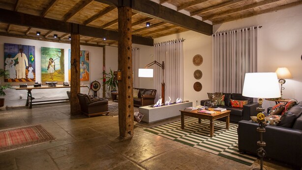 A spacious living area with a fireplace, a sofa, a coffee table, and a dining area with a table and chairs. - Pousada Armazem 26 (Tiradentes)