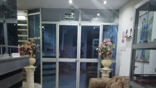 A reception area with a sofa, a glass cabinet, and a sign that reads "SALIDA". - Hospedaje Harjeny (Trujillo)