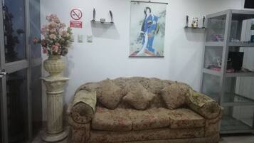 A room with a floral-patterned sofa, a vase with flowers, a framed picture of a person in traditional attire, and a cabinet with various items.