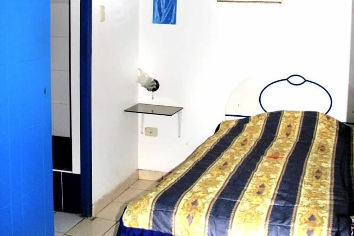 Quarto com cama, ventoinha no teto, mesa de cabeceira pequena e quadro pendurado na parede.