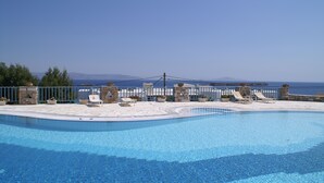 A swimming pool with lounge chairs and a stone wall, overlooking a clear blue sky and distant mountains. - Captains Rock (Paros)