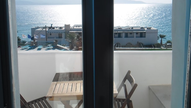 A balcony with a table and two chairs, overlooking a coastal area with buildings and a view of the sea. - Captains Rock (Paros)