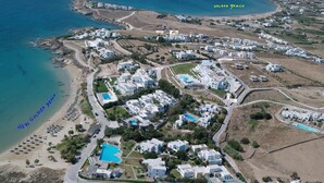 An aerial view of a coastal resort with villas, a beach, and a pool. - Captains Rock (Paros)