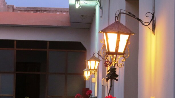 A building exterior with two wall-mounted lanterns and red flowers in front. - Gran Hotel (Arequipa)