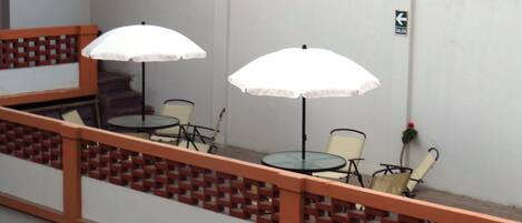 A balcony with two white umbrellas, a table, and two chairs.