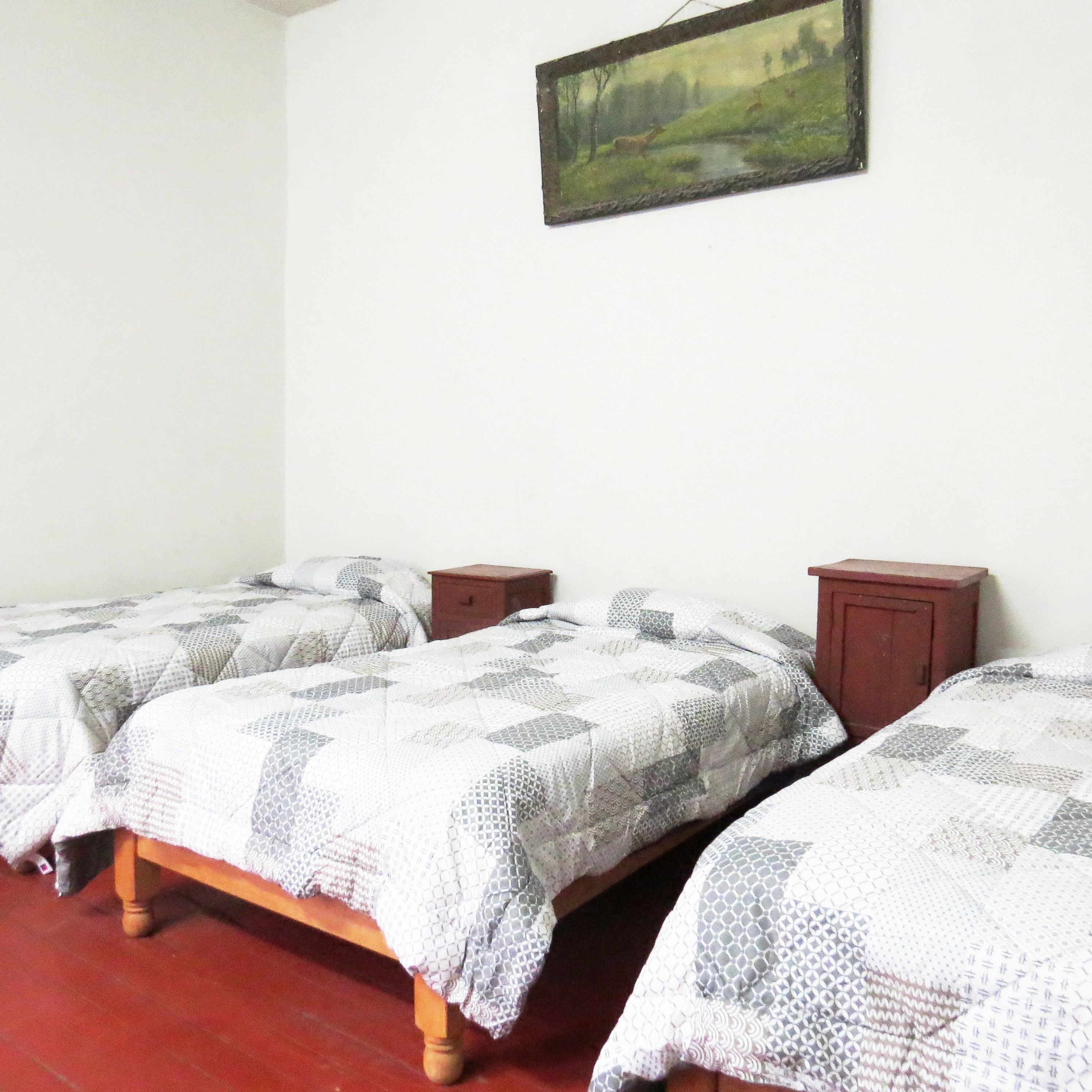 A bedroom with two single beds, a wooden nightstand, and a painting on the wall.