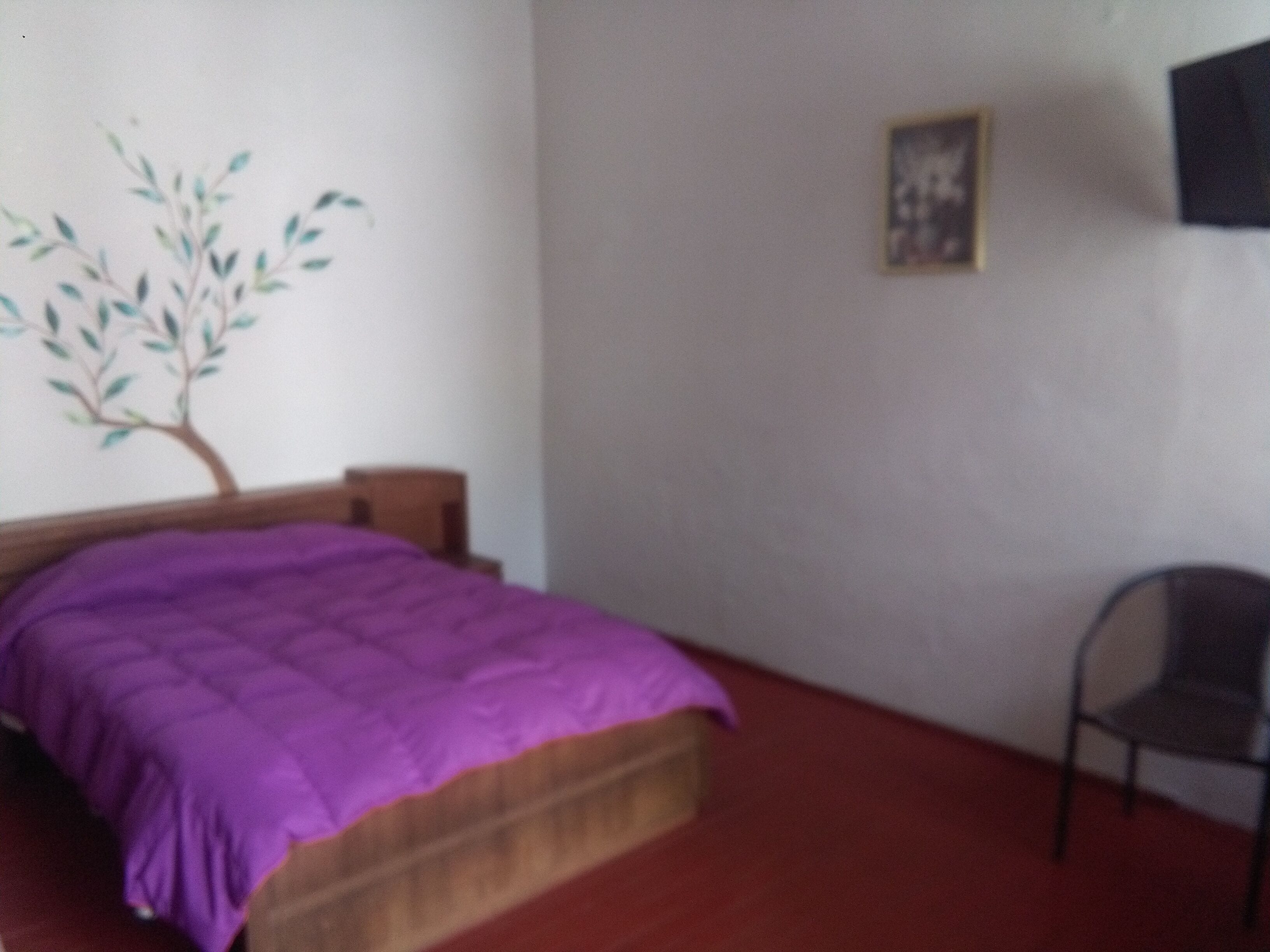 A bedroom with a bed, a chair, a wall-mounted TV, and a wall decoration.