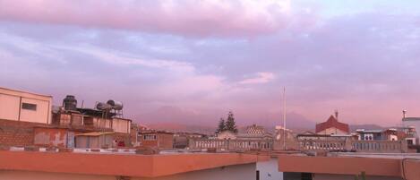 A rooftop terrace with a view of buildings and a cloudy sky.
