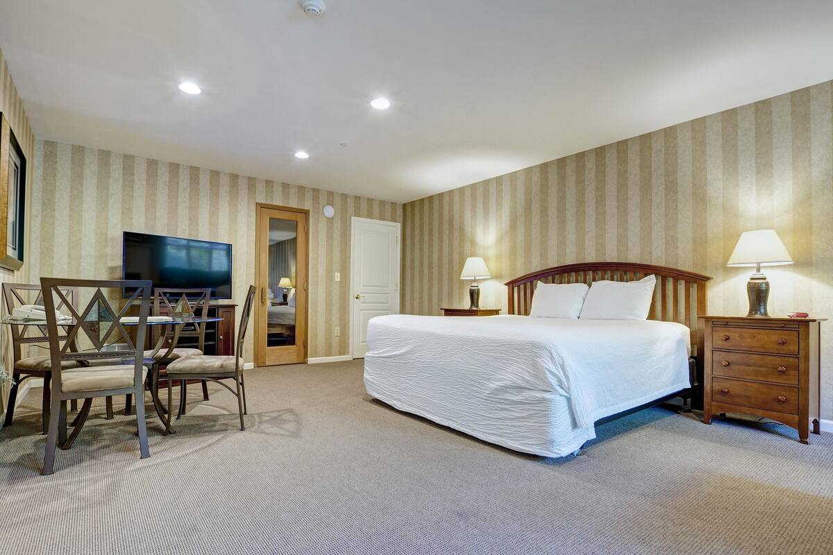 Une chambre d’hôtel comprenant un lit, des tables de chevet, un téléviseur, un bureau avec des chaises et un papier peint à rayures.