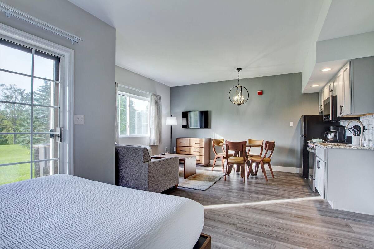 Une chambre moderne avec un grand lit, un bureau et un coin repas avec des chaises.