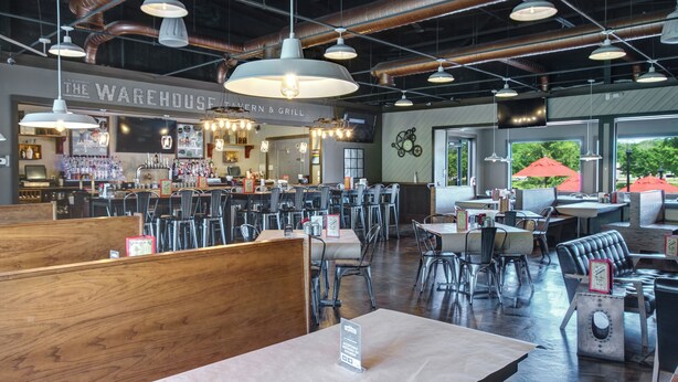 Un restaurante espacioso con techos altos, conductos expuestos y diferentes opciones de asientos, incluyendo cabinas y mesas.