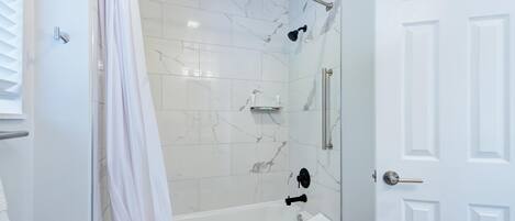 A modern bathroom with a glass-enclosed shower, white marble tiles, and a white door.