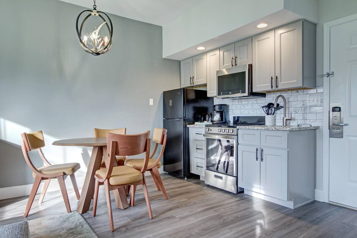 Une cuisine moderne avec des meubles blancs, des appareils en acier inoxydable et un coin repas doté de chaises en bois.