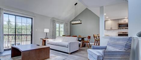 A modern living room with a sofa, a coffee table, a striped armchair, and a dining area with a table and chairs.