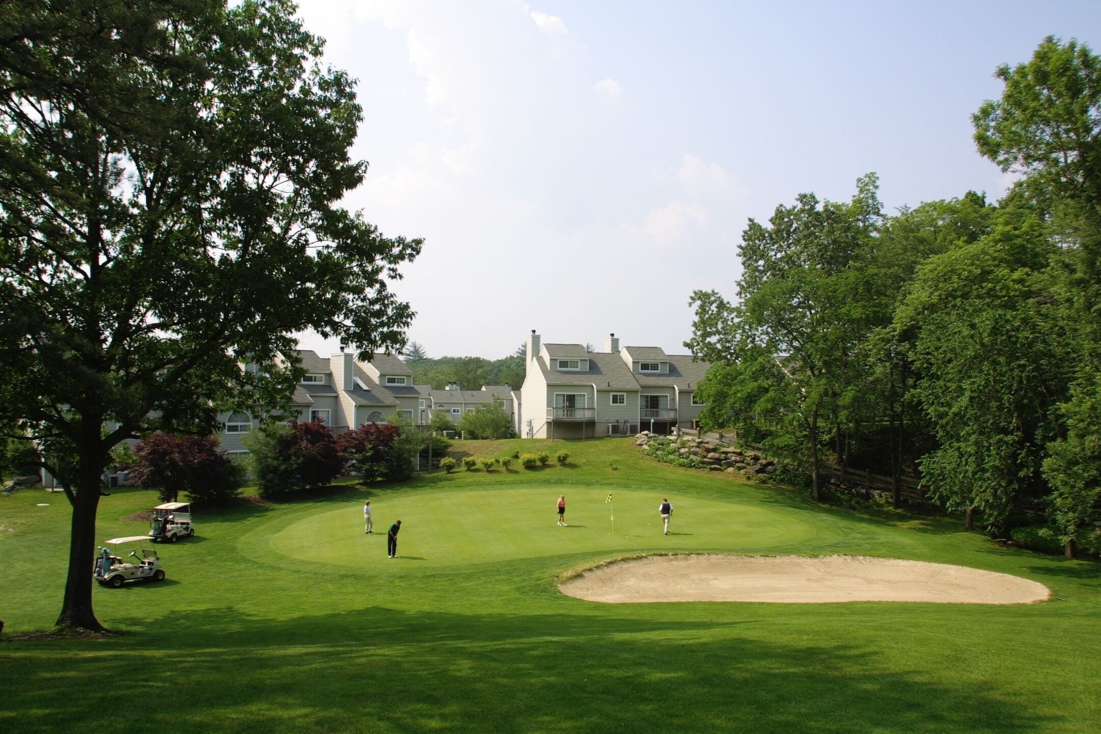 Een golfbaan met clubhuis, bomen en een zandbunker.