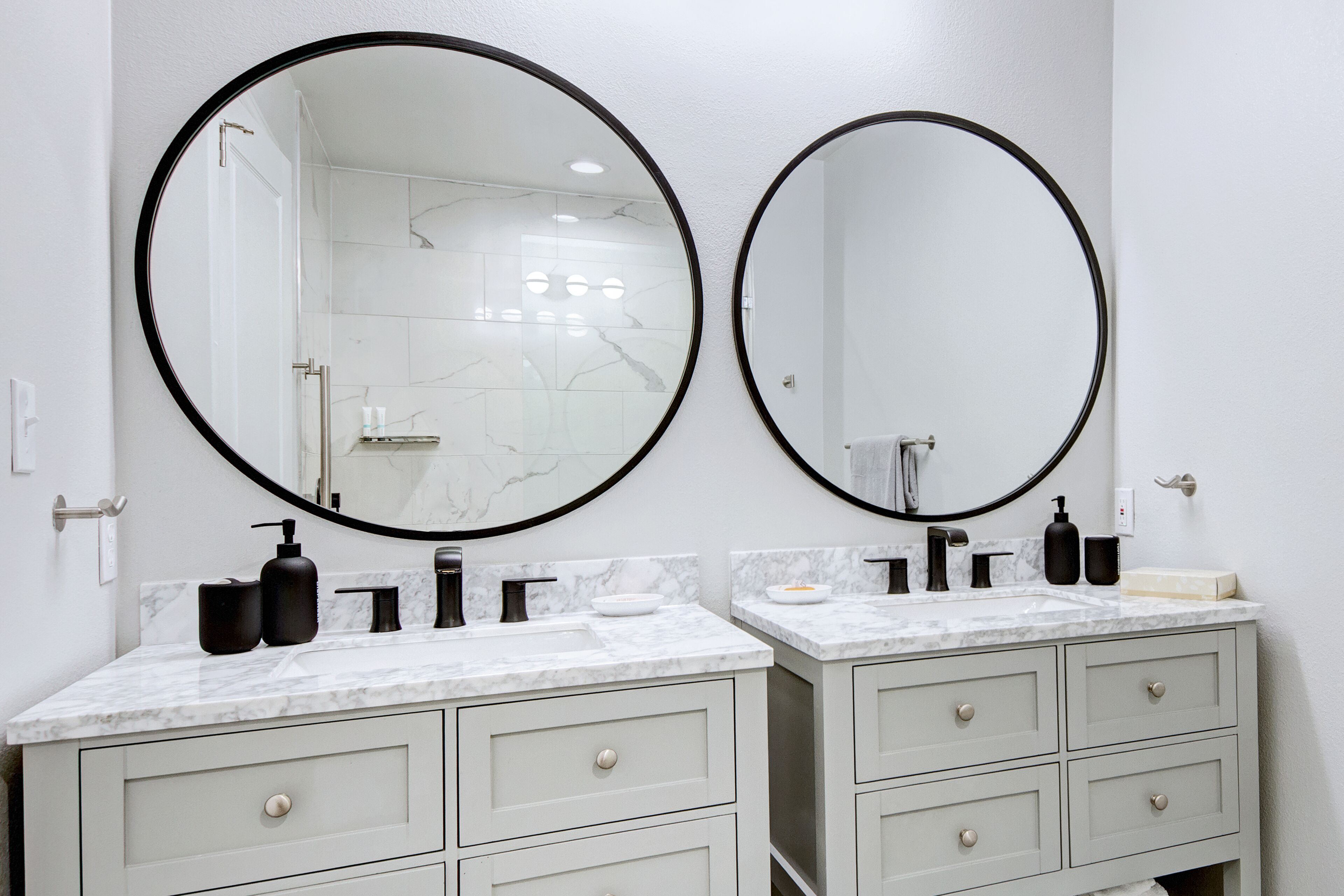 A bathroom with two sinks, each with a large mirror and a marble countertop. There are two drawers below each sink.