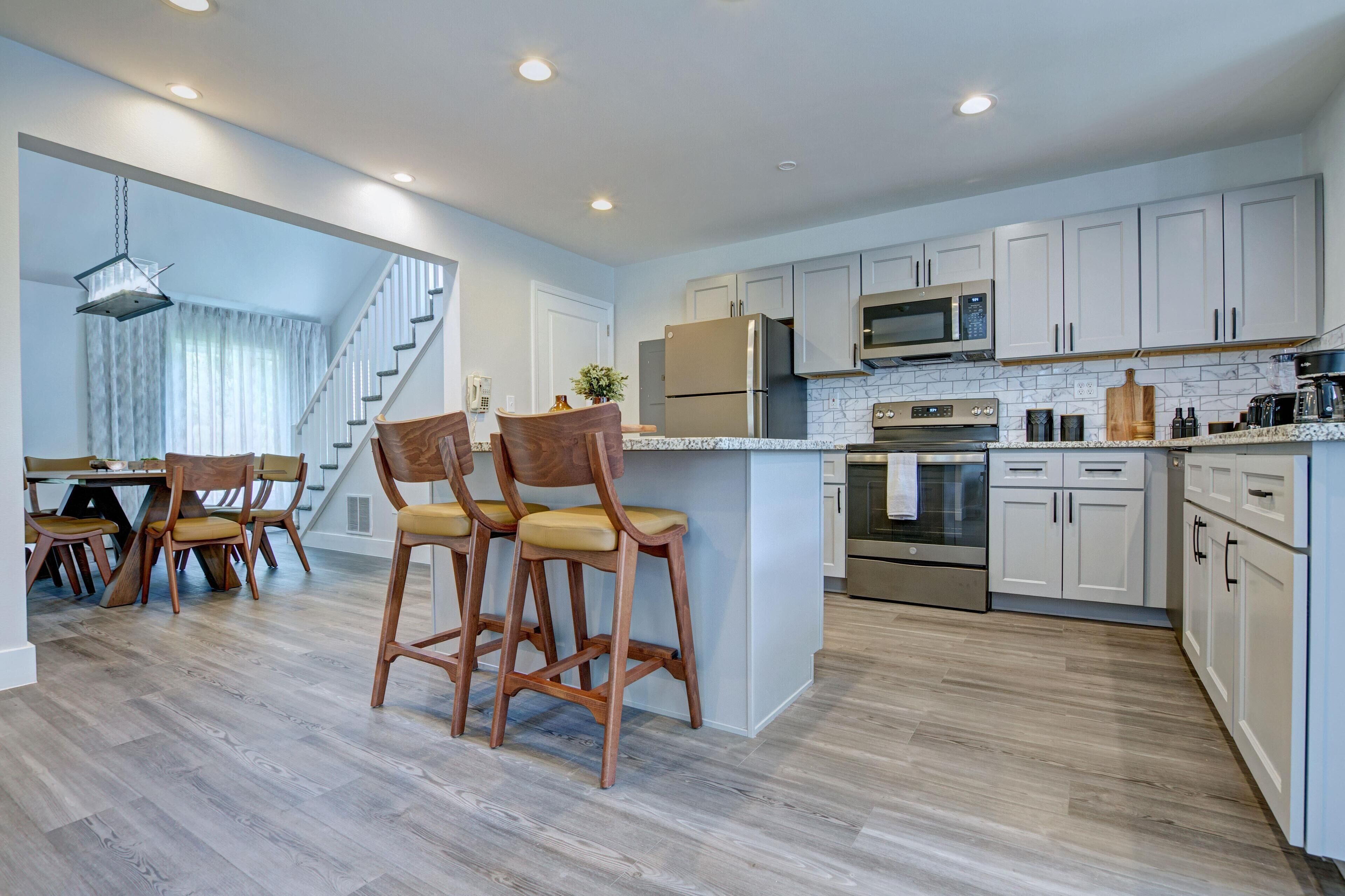 A modern kitchen with white cabinets, stainless steel appliances, and a wooden island with bar stools.