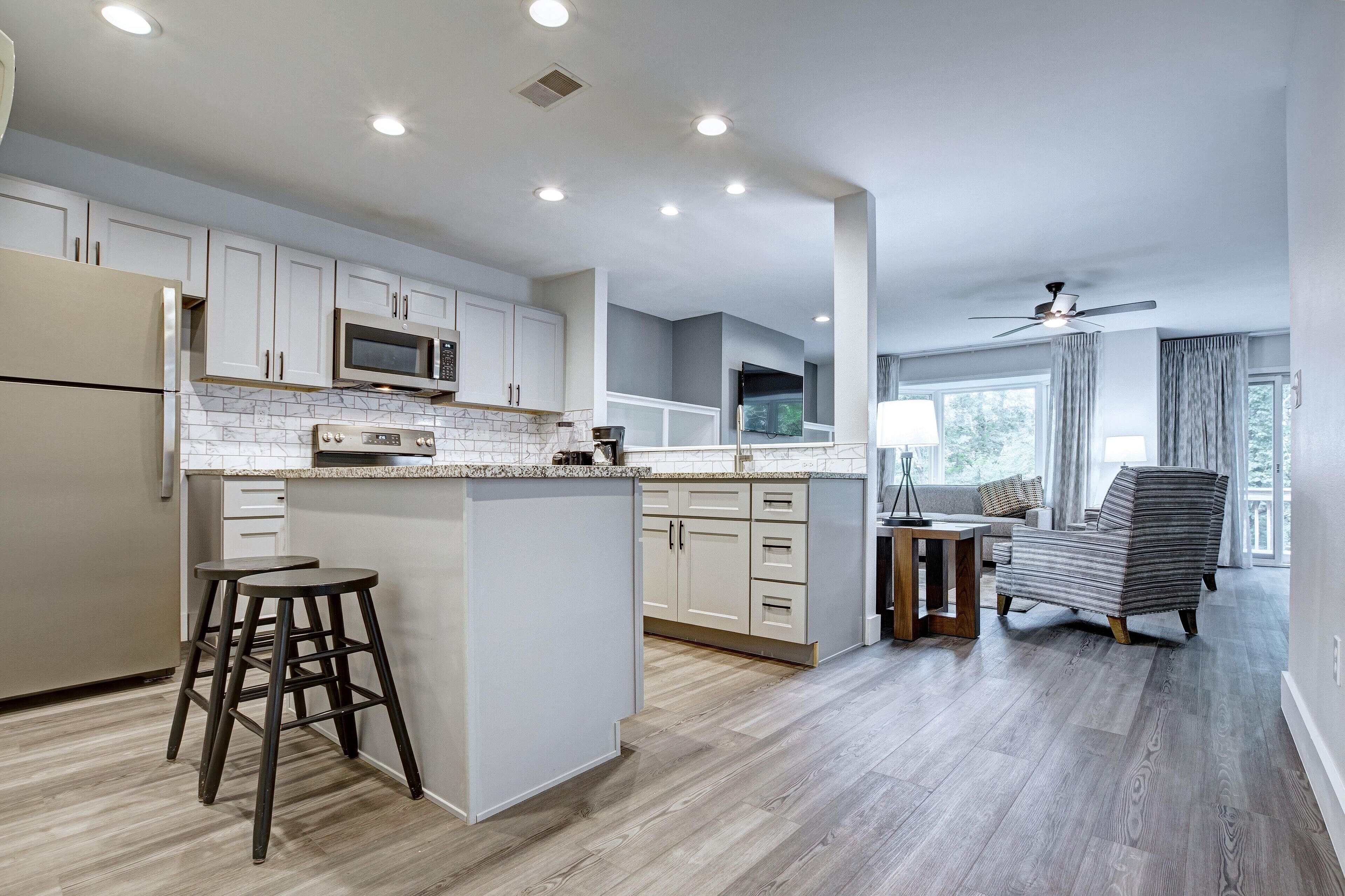 A modern kitchen with white cabinets, a central island, and a dining area with a sofa and a chair.