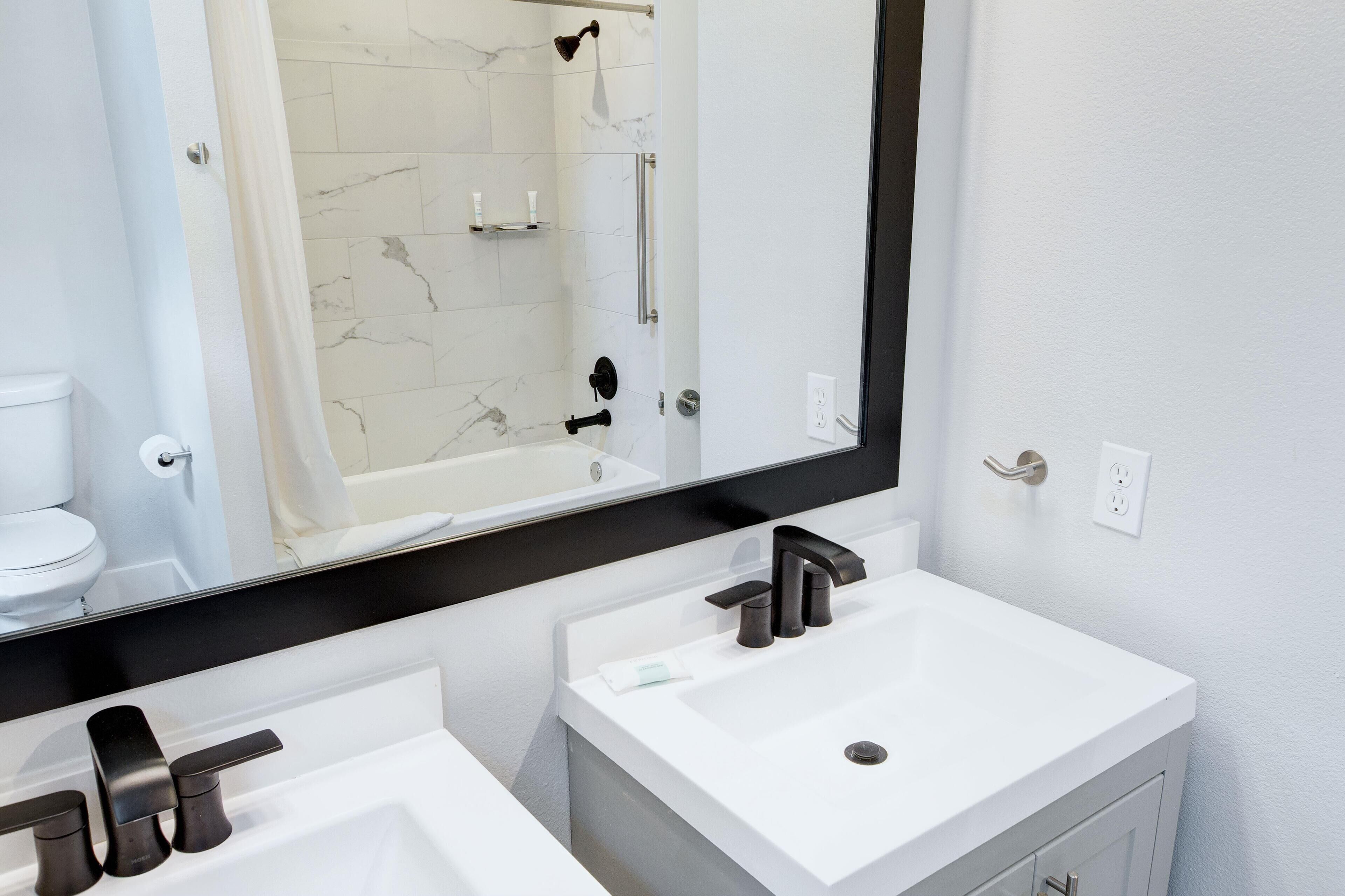 A modern bathroom with a white sink, a large mirror, and a shower area.
