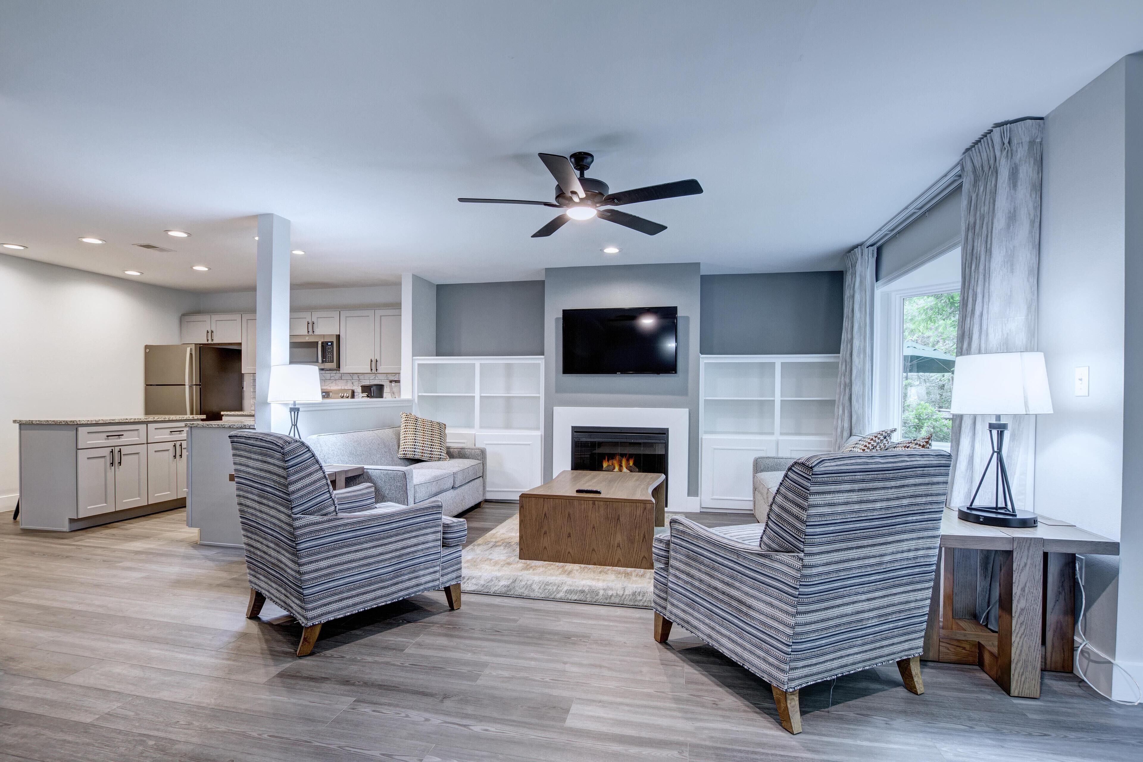 A modern living room with a fireplace, a television, and a ceiling fan.