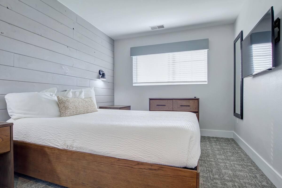 Une chambre à coucher avec un lit en bois, une table de chevet, une commode et une fenêtre avec des stores.