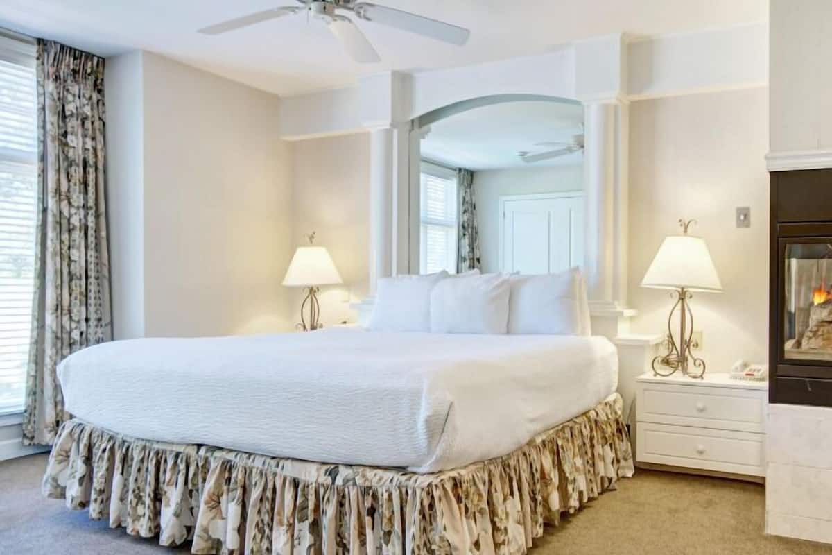 Un grand lit avec un couvre-lit à motifs floraux, deux lampes de chevet, un ventilateur de plafond et une cheminée.