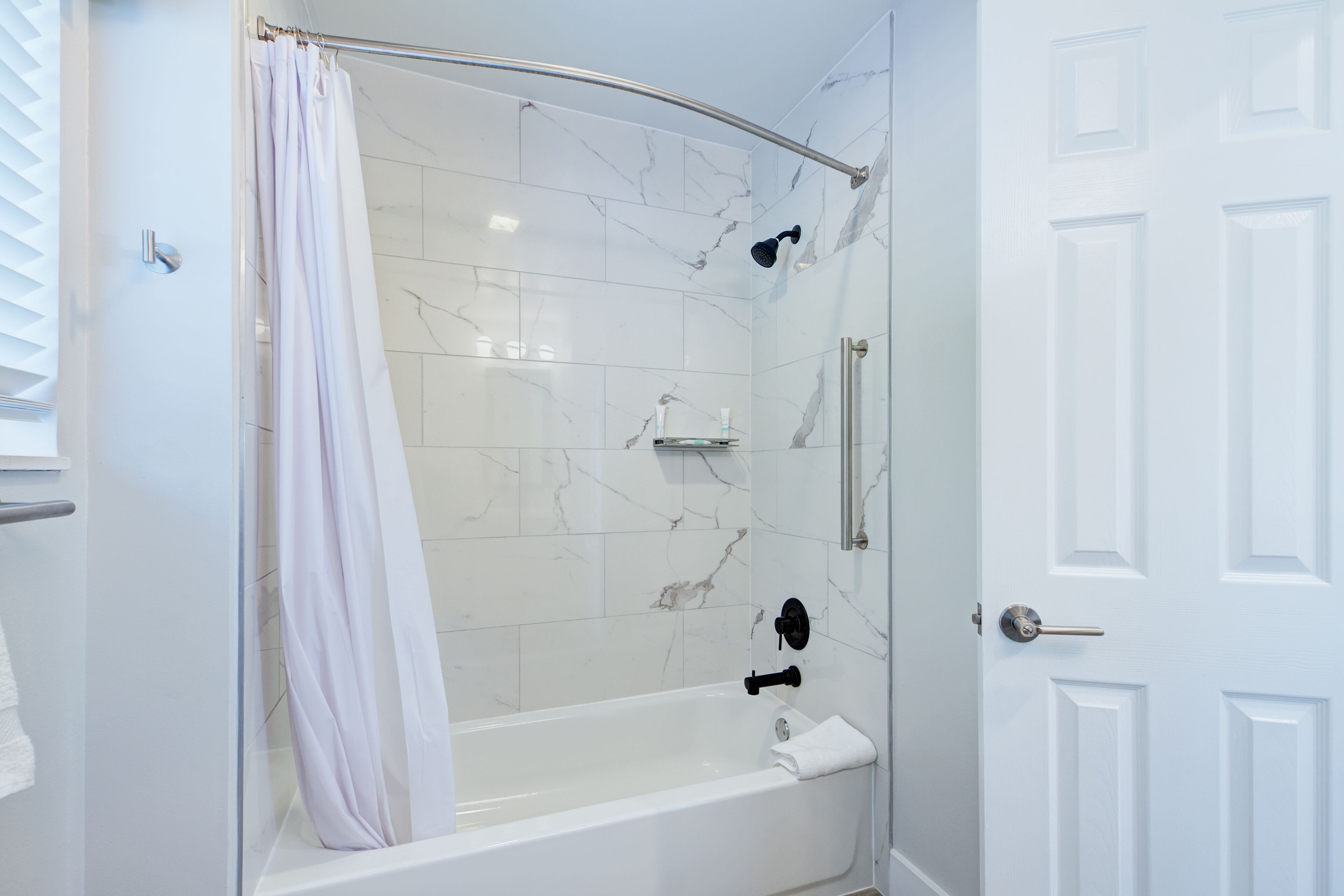 A modern bathroom with a glass-enclosed shower, white marble tiles, and a white door.