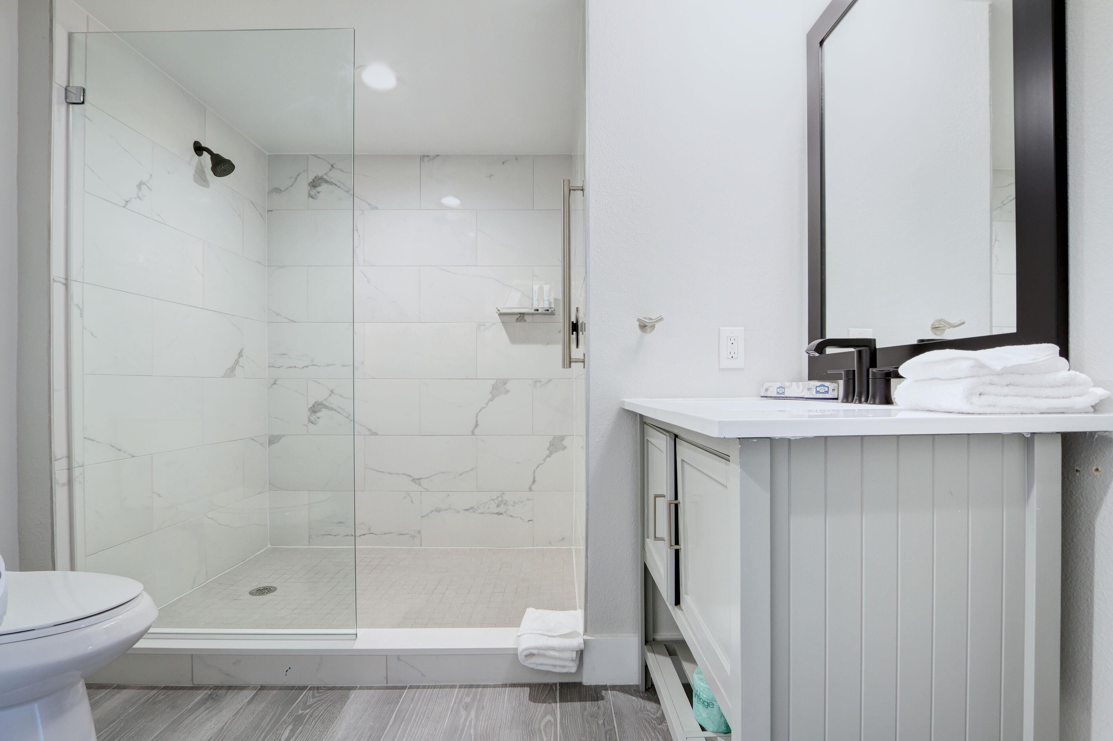 Un baño moderno con ducha envuelta en vidrio, inodoro blanco y tocador con espejo.