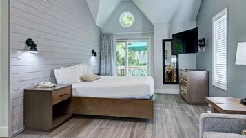 A bedroom with a bed, bedside table, lamp, TV, and a view of the outdoors.
