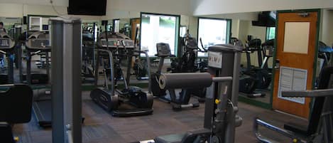 Ein Fitnessstudio mit verschiedenen Trainingsgeräten, einem Spiegel und einem Ausgangsschild.