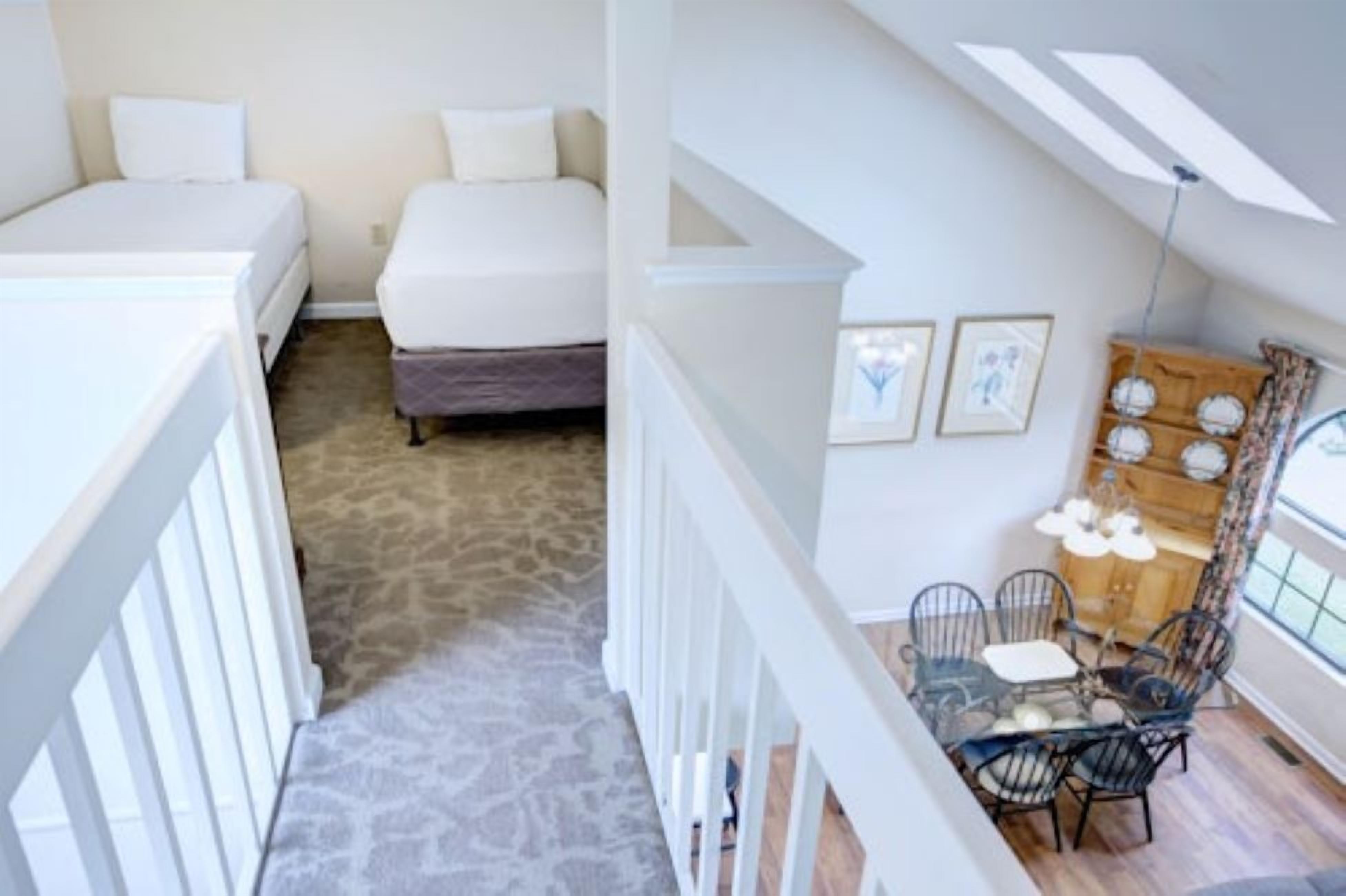 A bedroom with two beds, a dining area with a table and chairs, and a staircase.