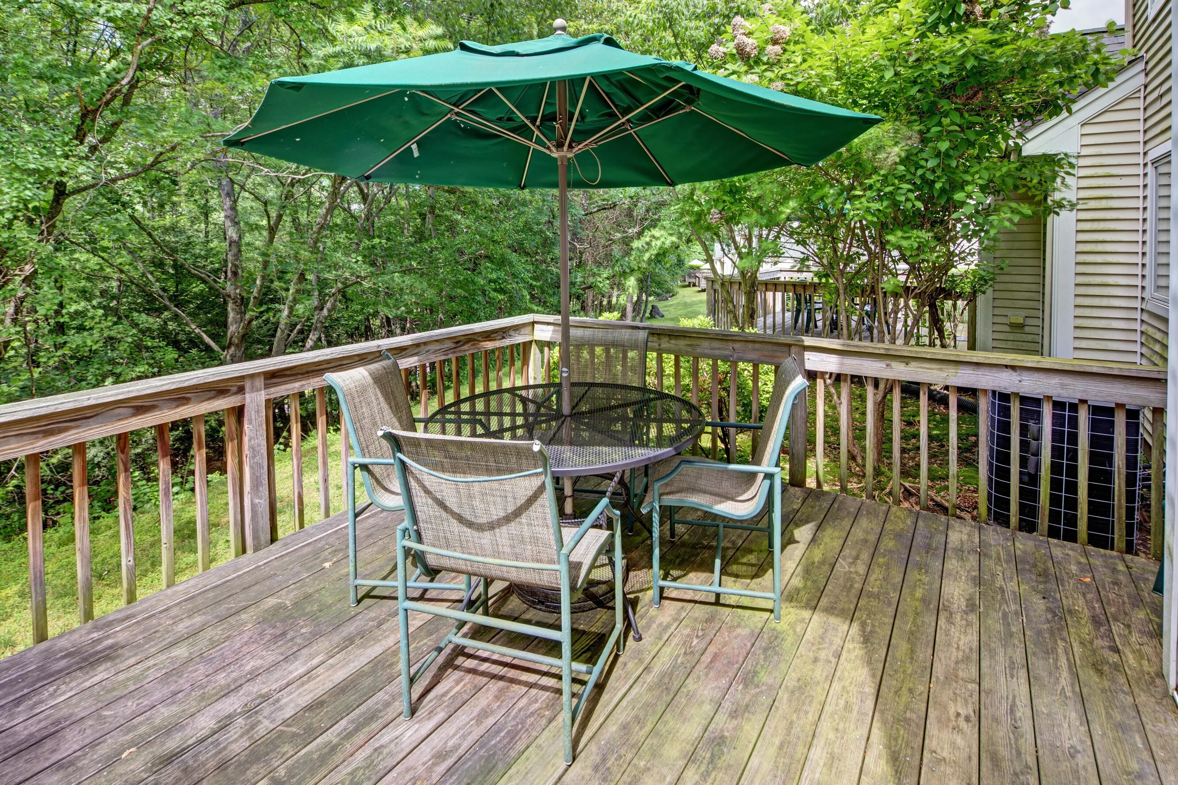 A wooden deck with a round table and chairs, an umbrella, and a railing.