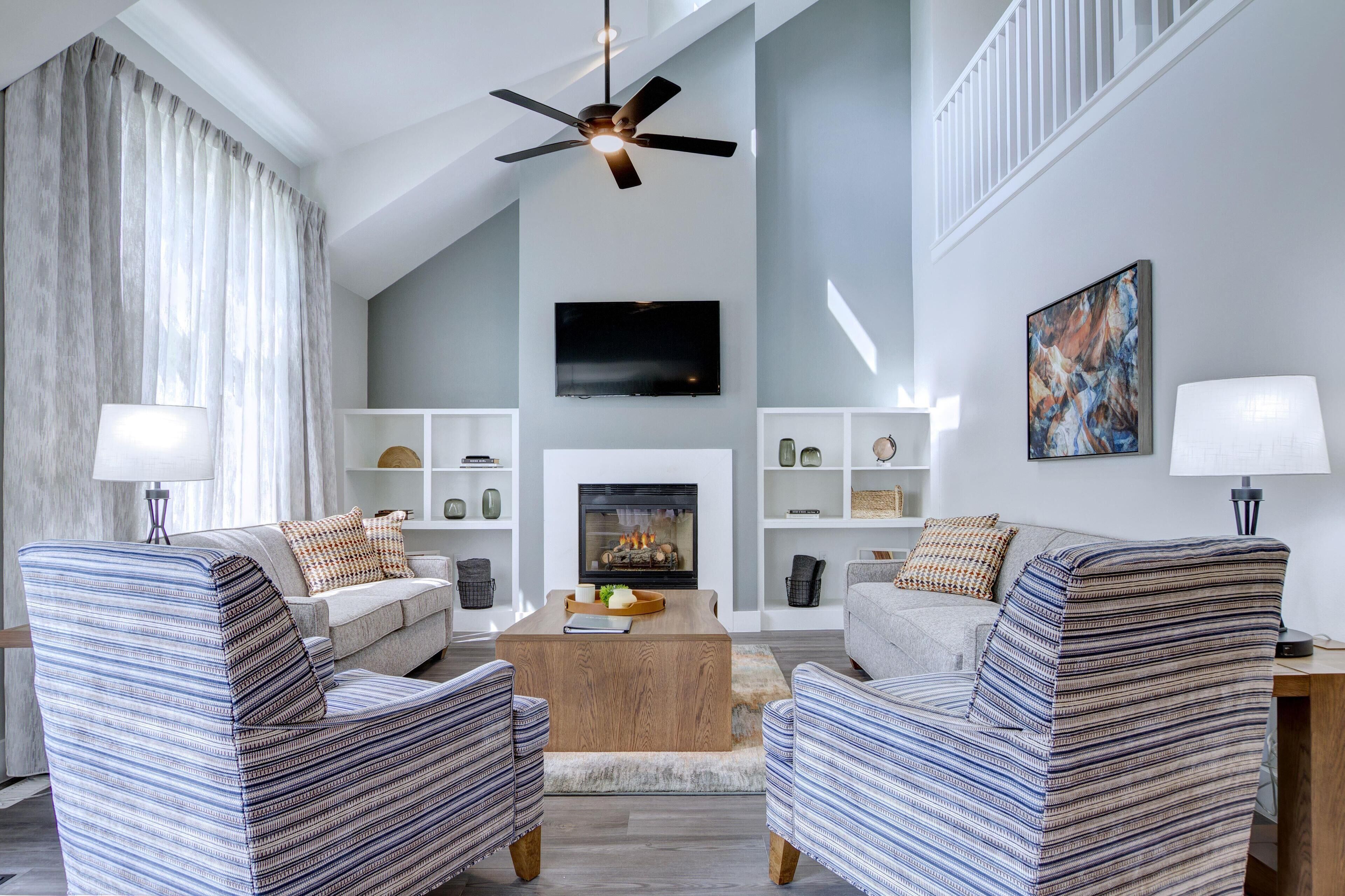 A modern living room with a fireplace, two sofas, a coffee table, and a ceiling fan.