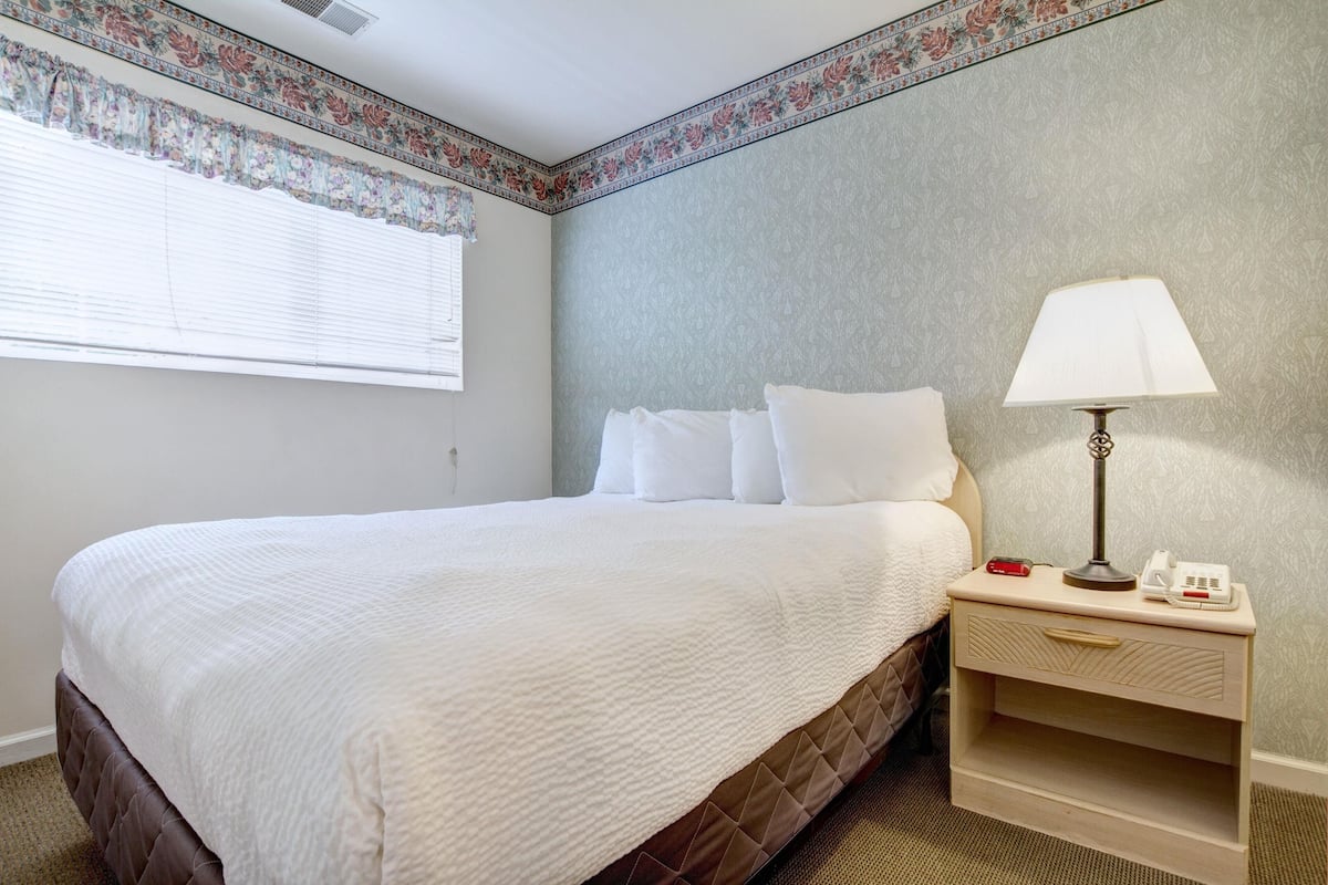 Un lit bien fait, avec du linge de lit blanc, une table de chevet avec une lampe et une bordure à motifs floraux sur le mur.