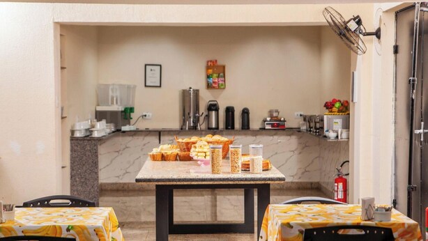 A small kitchen area with a marble countertop, a table with a fruit pattern tablecloth, and a basket of pastries. - Londres Royal Hotel (Londrina)